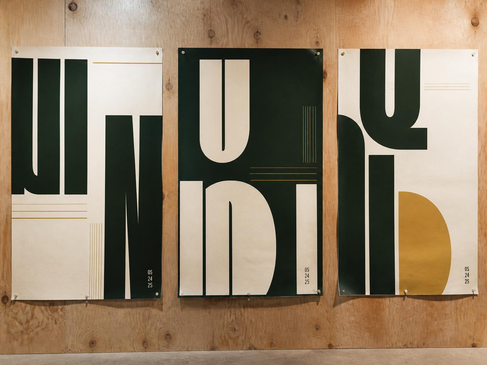 Three large-format typographic promotional posters pinned to a plywood studio wall